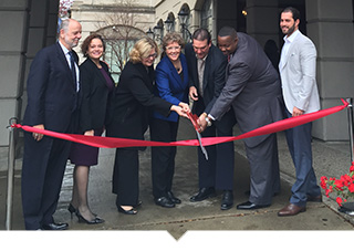 Group holding large scissors cutting the ribbon at the opening of the Regis Houze apartment building in Detroit