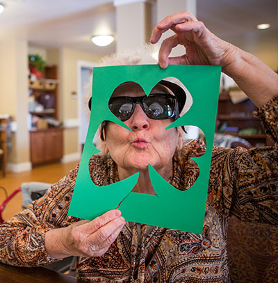 Older adult woman makes funny face through cutout of shamrock