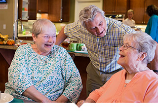 Three older adults talk and laugh at table.