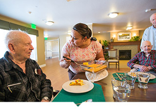 Worker serves meal to older adult man at table