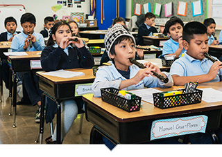 elementary school kids play musical instruments at their desk in a classroom