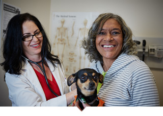 Patient poses with small dog on lap while being examined by doctor at community health center