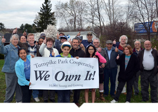 Large group of people pose together holding sign outside of the manufactured housing community that reads We Own It