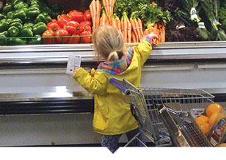 Little girl reaches up to grab fresh produce