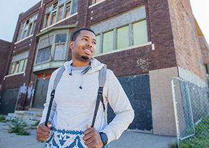 Young male stands in front of abandoned building.