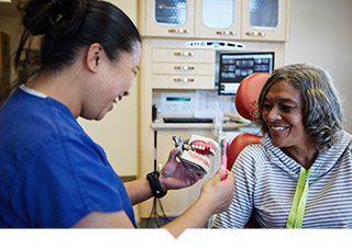 Text: Dentist uses model of teeth to show patient proper brushing technique