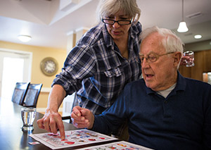 Care giver helps older man in assisted living community play bingo.