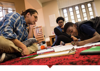 A charter school teacher works with a student on the floor of the classroom