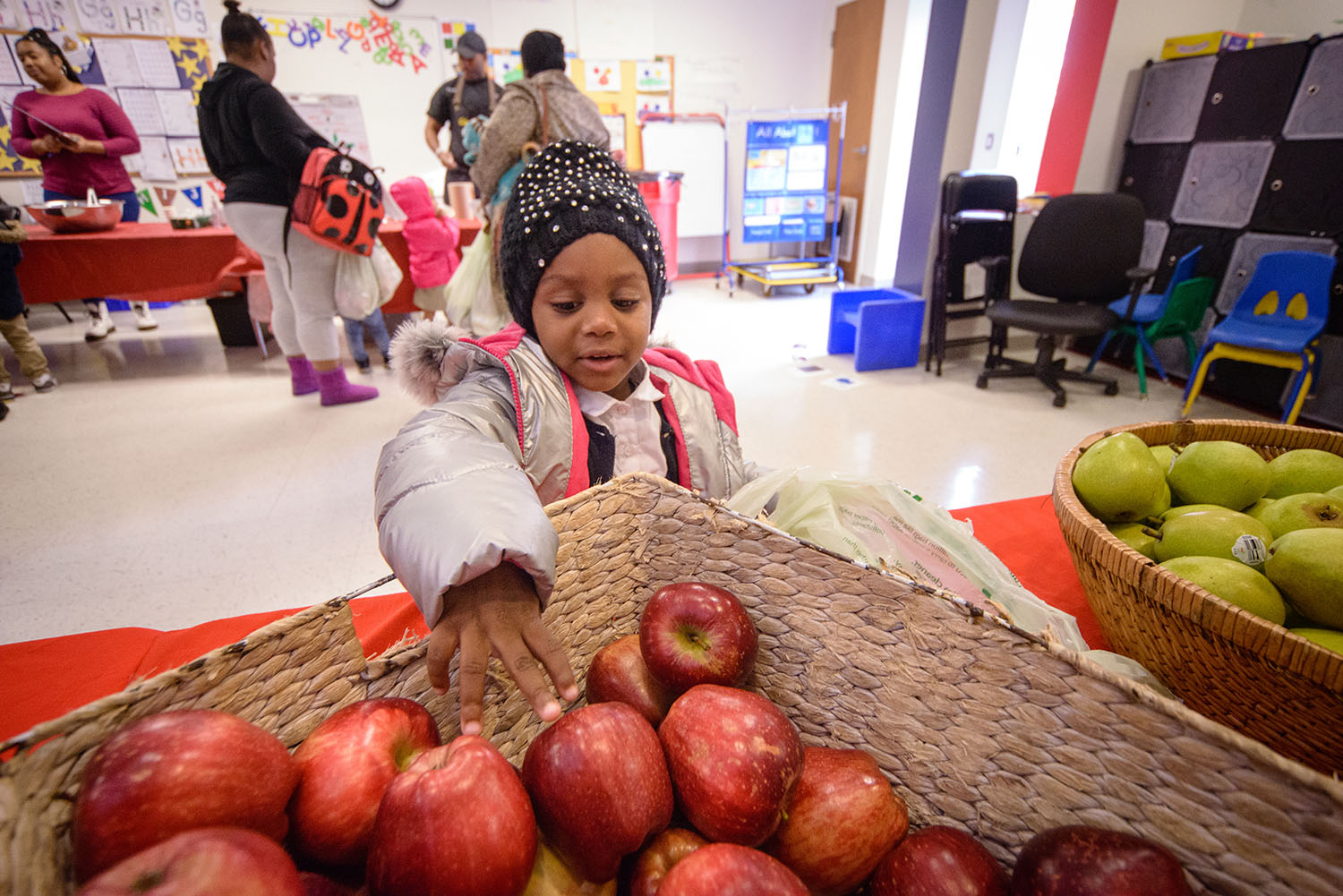 A little girl reaches for an apple.