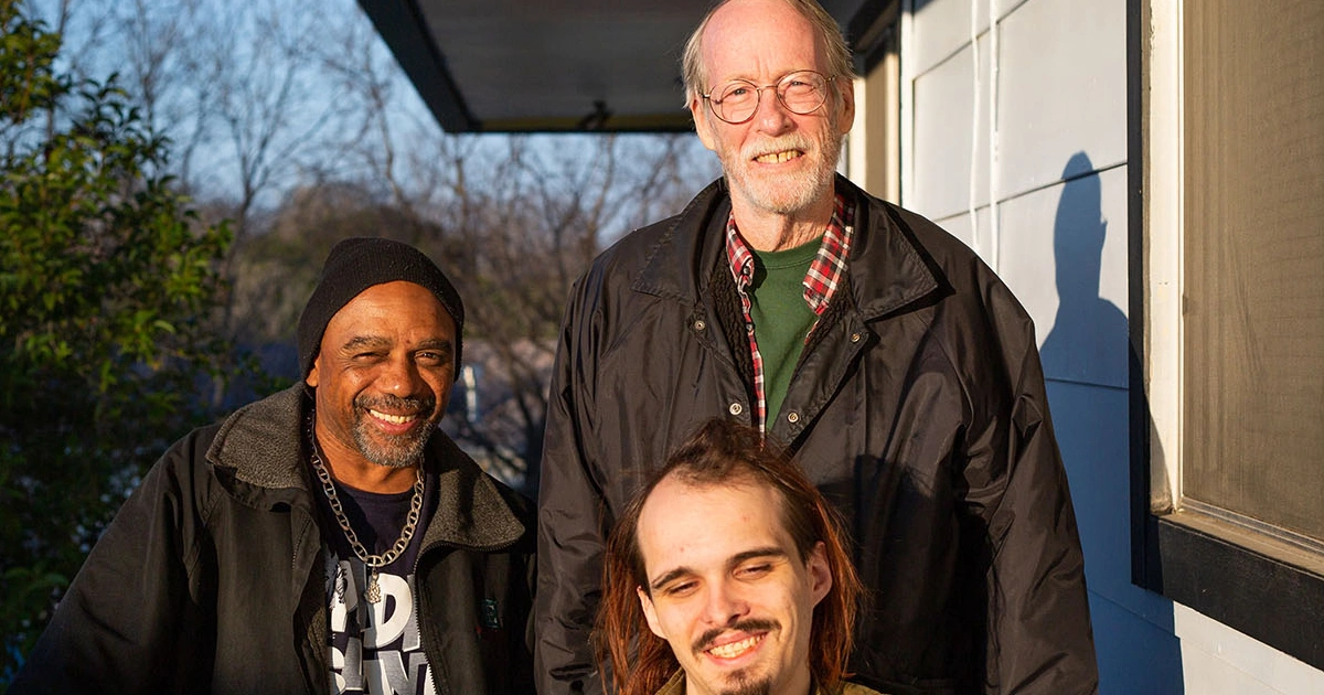Three La Reunion housing coop residents pose outside of their apartments.