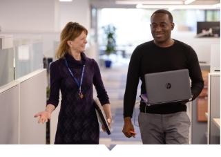 Two Capital Impact employees walk down office hallway together.