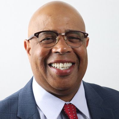 A photo of Gary Cunningham, the new chairman of the boards of directors of Capital Impact Partners and CDC Small Business Finance, shown smiling, wearing glasses, a blue suit, white dress shirt, and red tie.