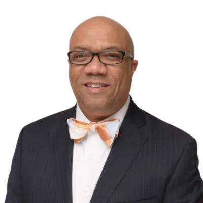 A photo of Gary Cunningham, the new chairman of the boards of directors of Capital Impact Partners and CDC Small Business Finance, shown smiling, wearing glasses, a blue suit, white dress shirt, and red tie.