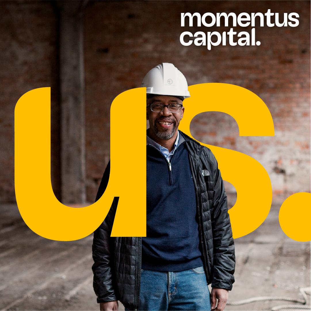 Real estate developer standing in hard hat in front of the word "us" with the Momentus Capital logo in the corner.