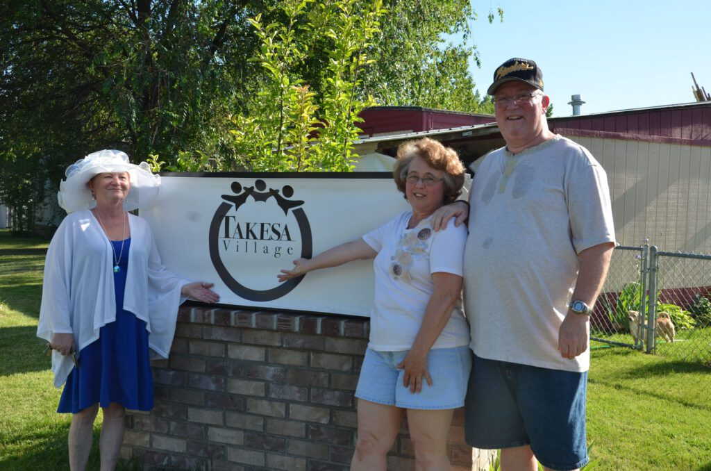 Residents of Takesa Village community point to their community sign