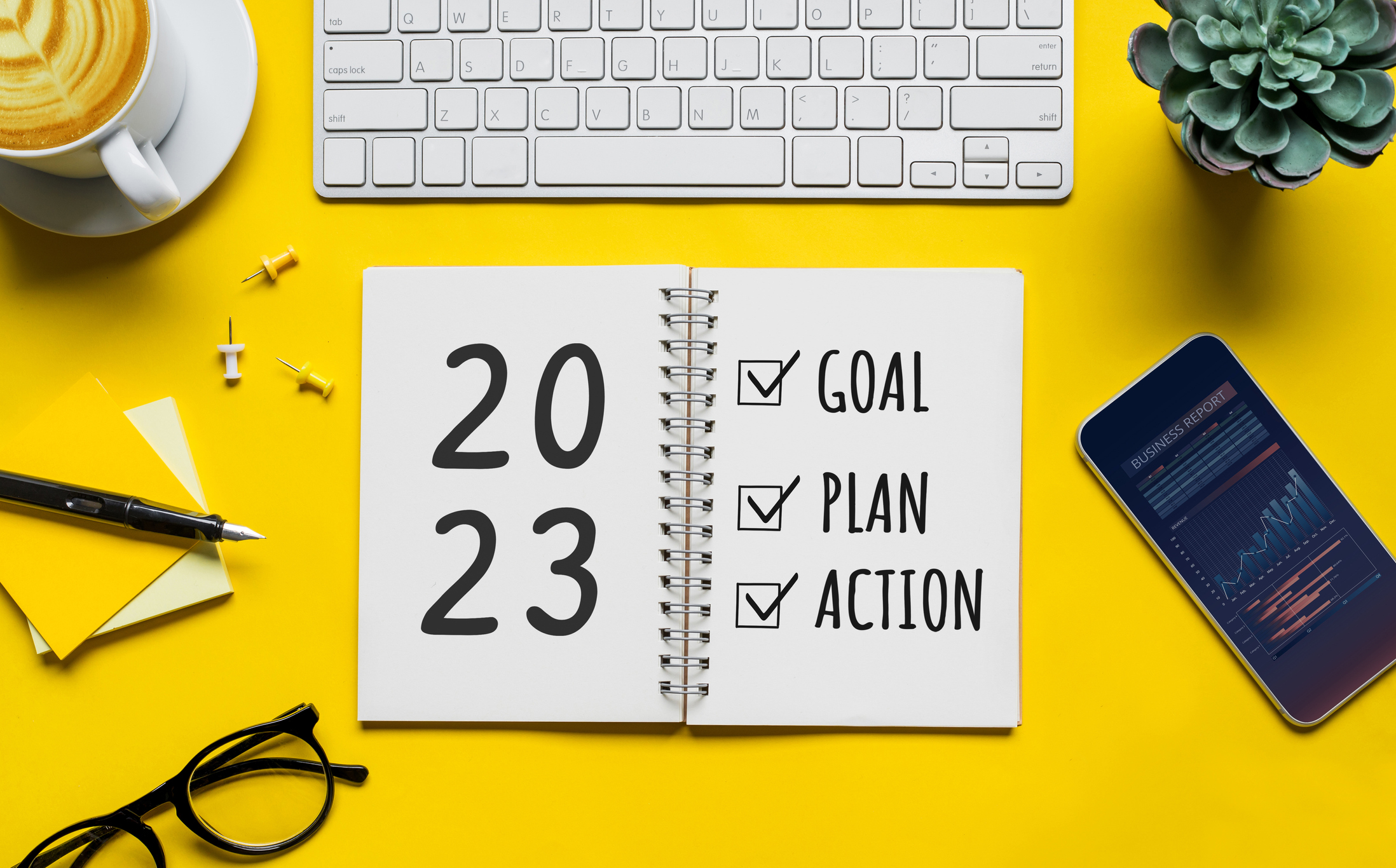 Graphic with a yellow background, computer, cell phone, and other office accessories with 2023 goals ahead.