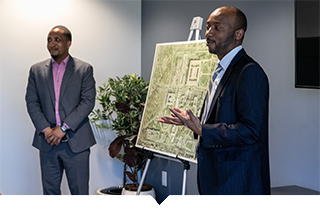 Black developer gives a presentation in front of an architectural drawing