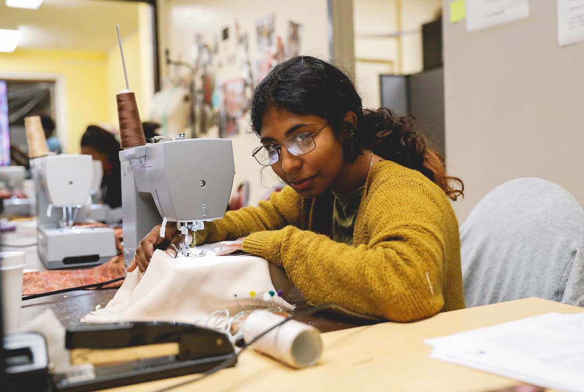 Woman at a sewing machine looks at the camera