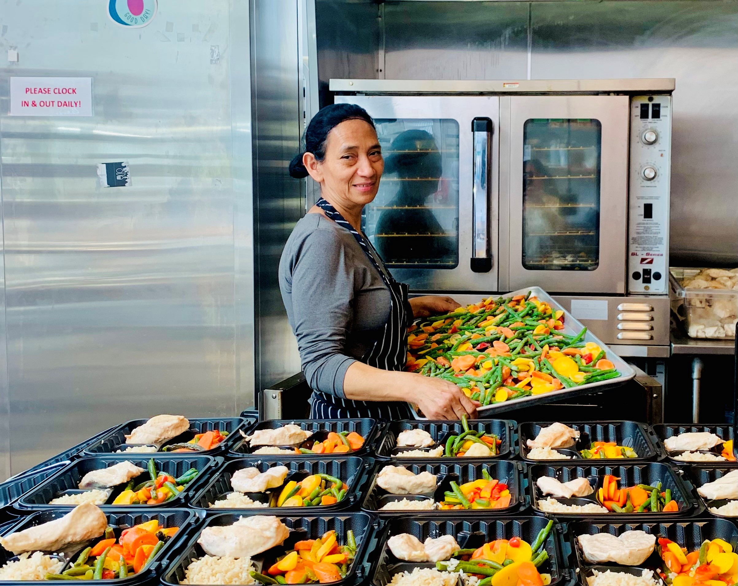 Woman in commercial kitchen holding a tray of vegetables in front of a cold storage refrigerator