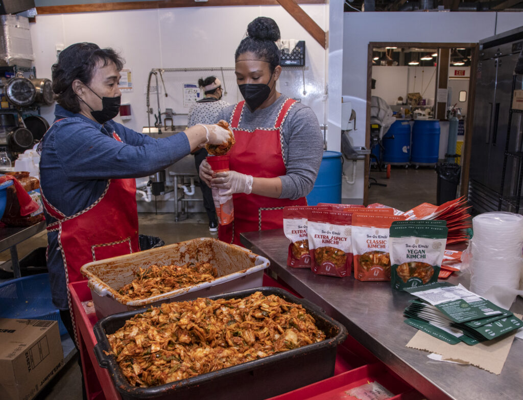 Two female food workers packaging food in a kitchen setting.