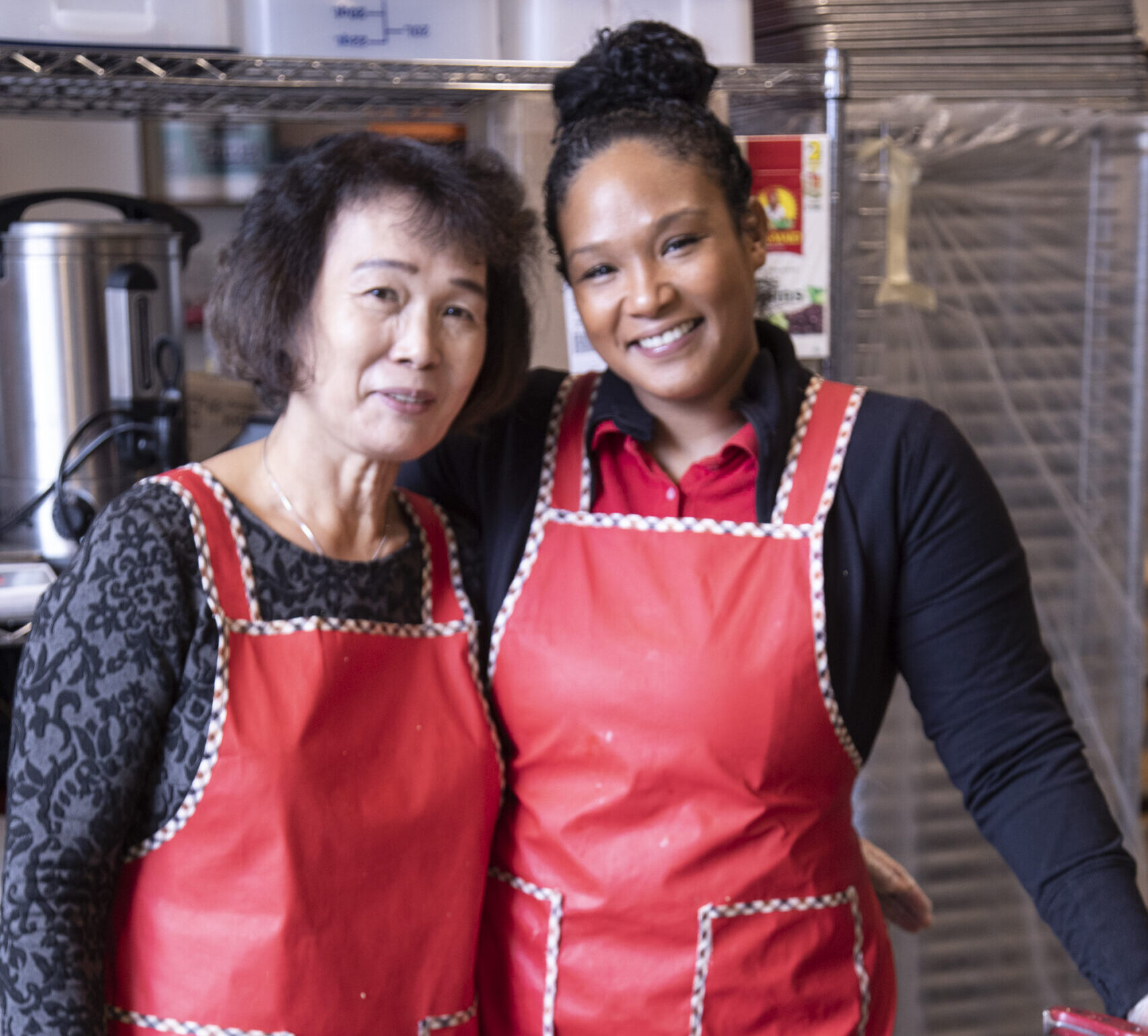 An Asian American and a Black woman working in the kitchen and smiling at the camera