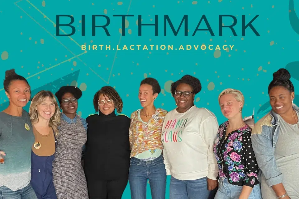 A diverse group of women from the Birthmark Doula Collective, one of Capital Impact Partners' 2023 Co-op Innovation Award recipients, post in front of a banner reading 'Birthmark Birth Lactation Advocacy'.