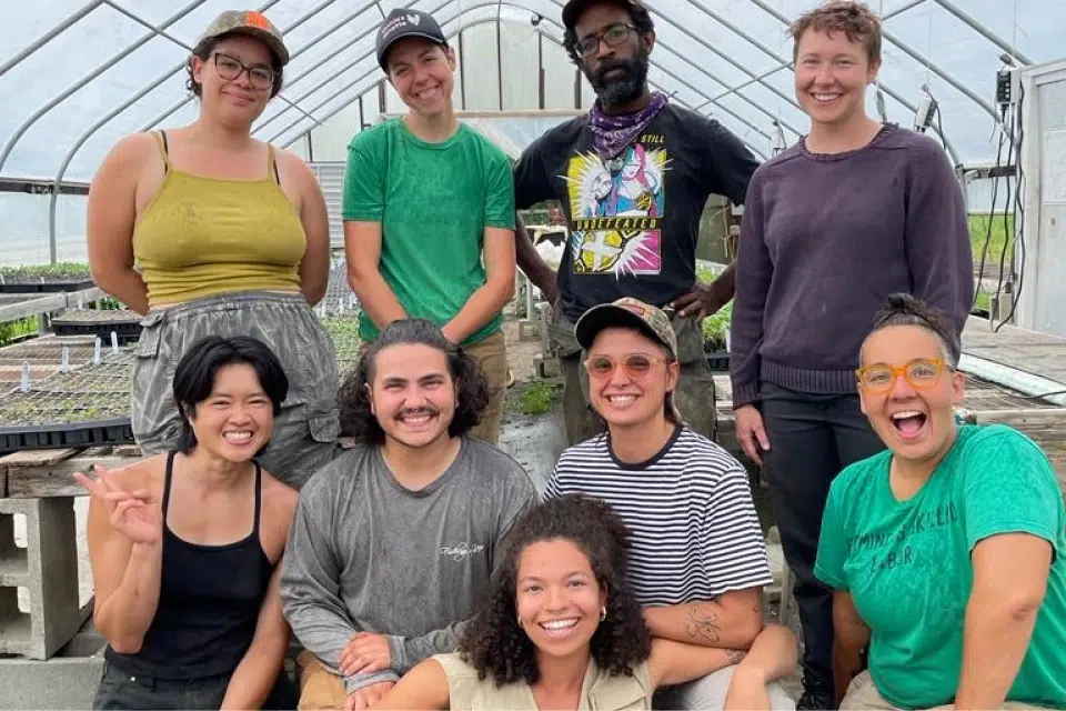 Rock Steady Farm members, a Co-op Innovations 2023 award recipient, smile and pose together inside a greenhouse.