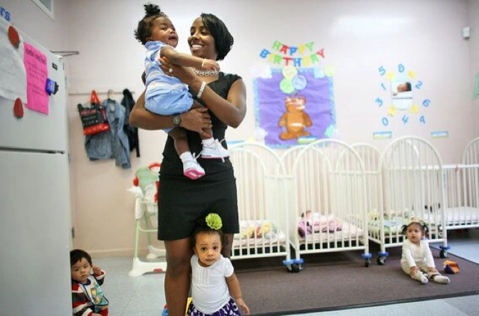 A woman holds a baby in a bright nursery, representing the warmth and community spirit of a childcare co-op.