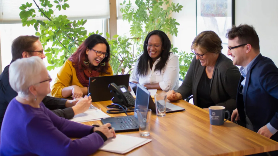A group of people with laptops gathered around a table, engaged in discussion and decision-making for their cooperative.