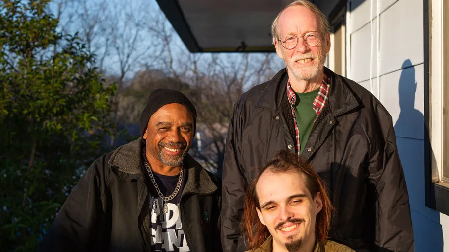 Three smiling men stand together, representing NASCO, a housing cooperative providing affordable housing solutions.