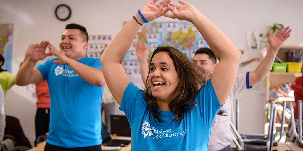 Classroom filled with adults with arms up, illustrating Briya's unique model for simultaneous learning for parents and children.