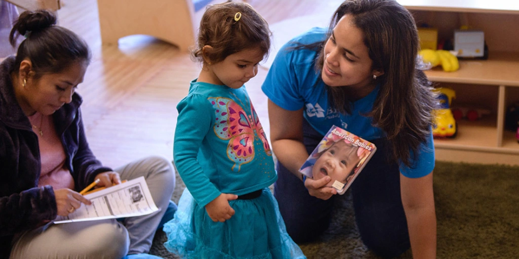 A woman and child sit on the floor surrounded by books, enjoying a learning moment together at Briya Public Charter School which offers a  unique “two-generation” educational model.