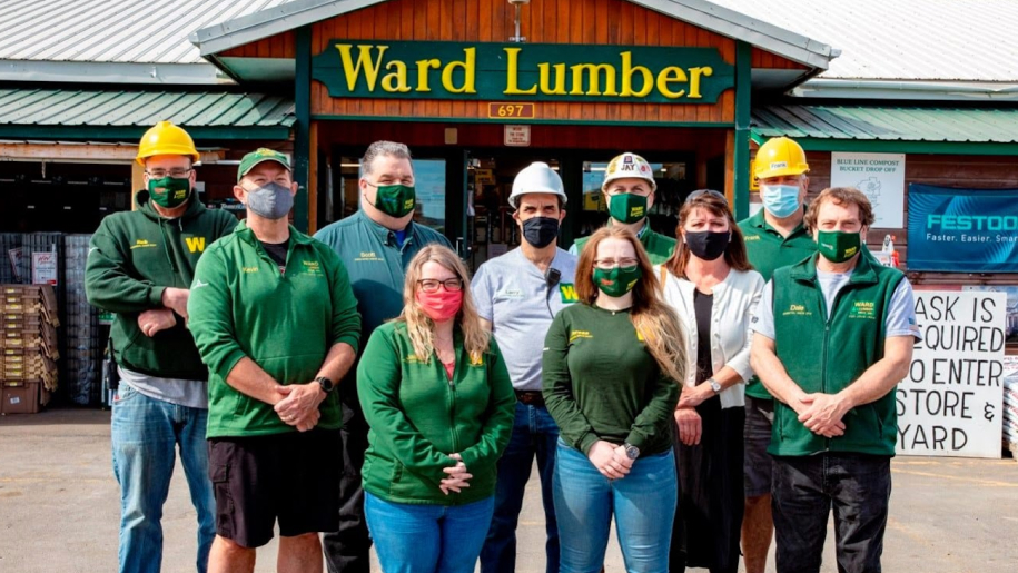 Employees of Ward Lumber, a worker cooperative supported by Capital Impact Partners, stand as a group in front of their building which has the company name on top.