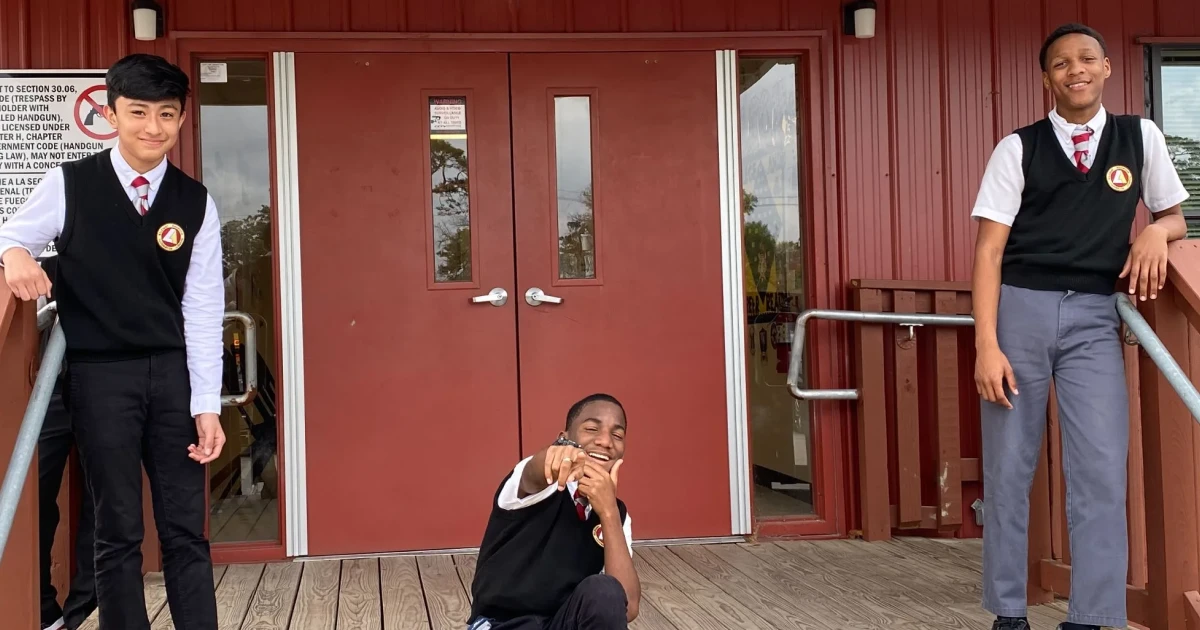 Three male students smile at the camera in front of a charter school financed by Capital Impact Partners.