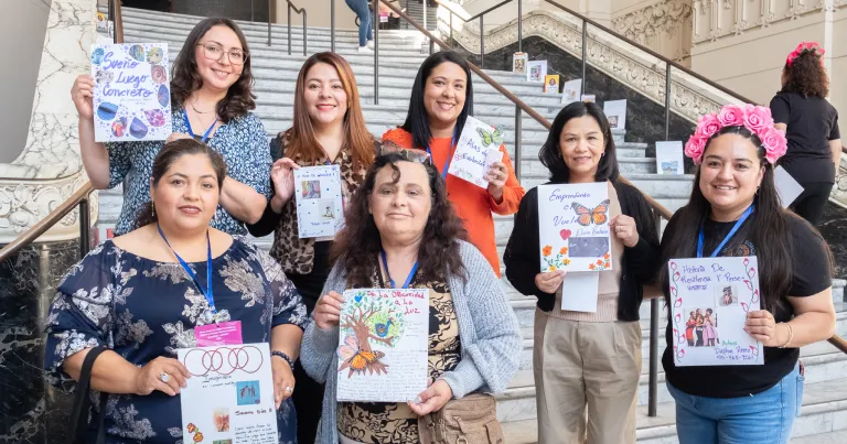Members of Prospera Community Development, a Capital Impact Partners 2025 Co-op Innovation Award winner pose together holding artwork advocating for economic independence and community entrepreneurship initiatives.